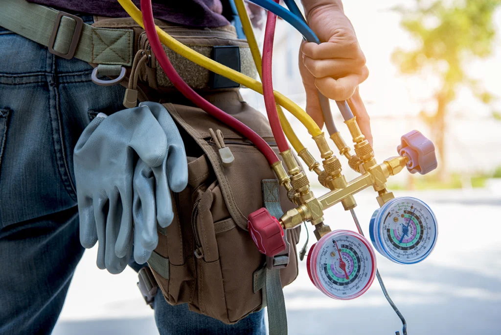 Close-up of HVAC manifold gauges and service hoses carried by a technician during an air conditioning service call.