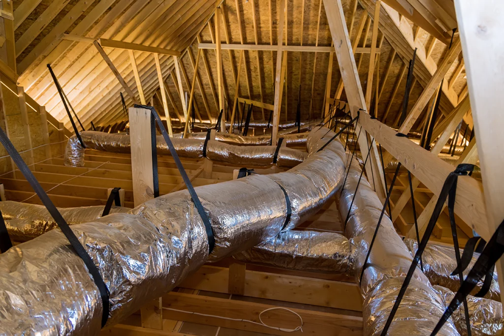 Exposed flexible HVAC ductwork installed in a residential attic with visible framing and support straps. Best for blogs about attic ductwork, duct installation, airflow issues, and residential HVAC systems.